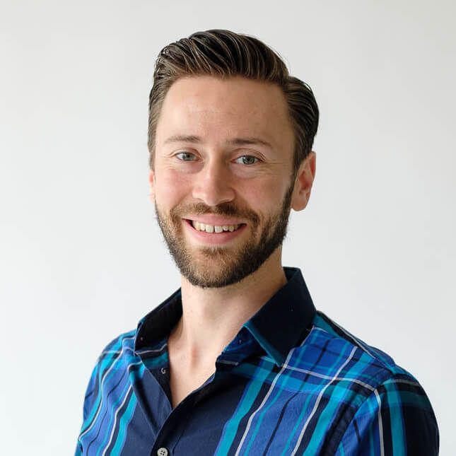 Portrait of a smiling man with a beard wearing a blue plaid shirt against a plain white background.