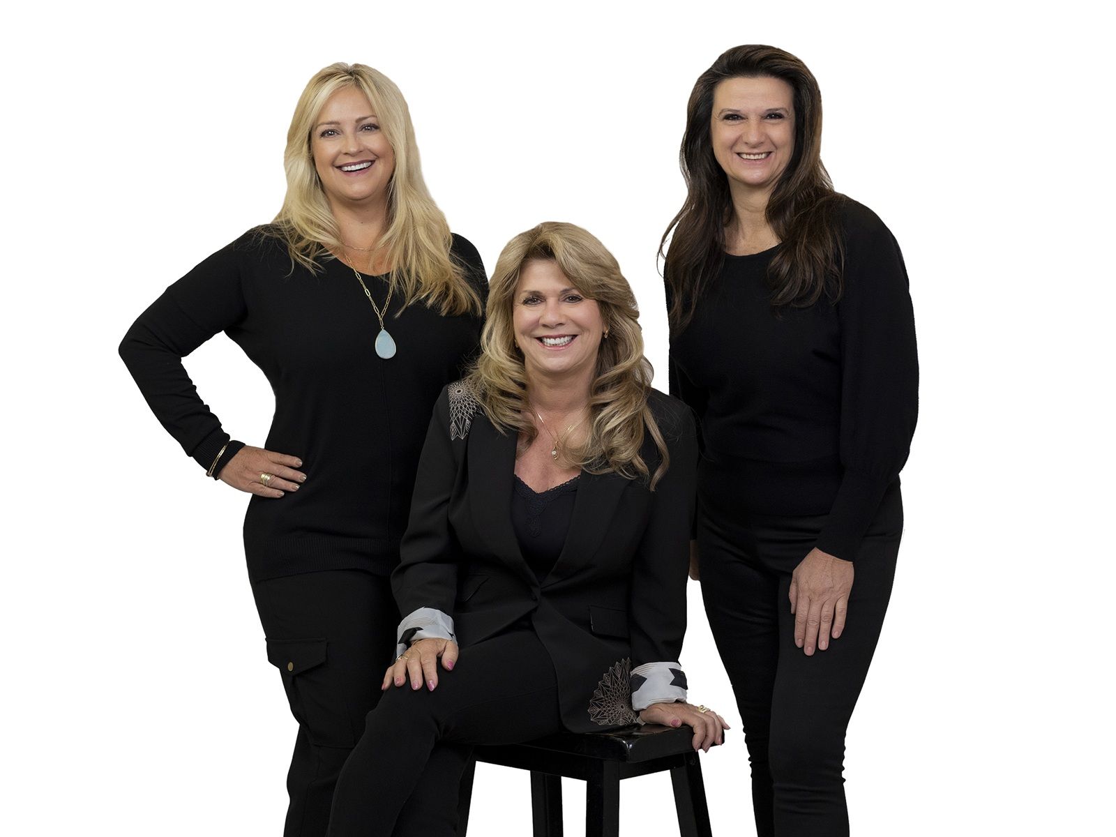 Group of four women with blonde and brunette hair wearing black outfits and sunglasses, posing together against a light background.