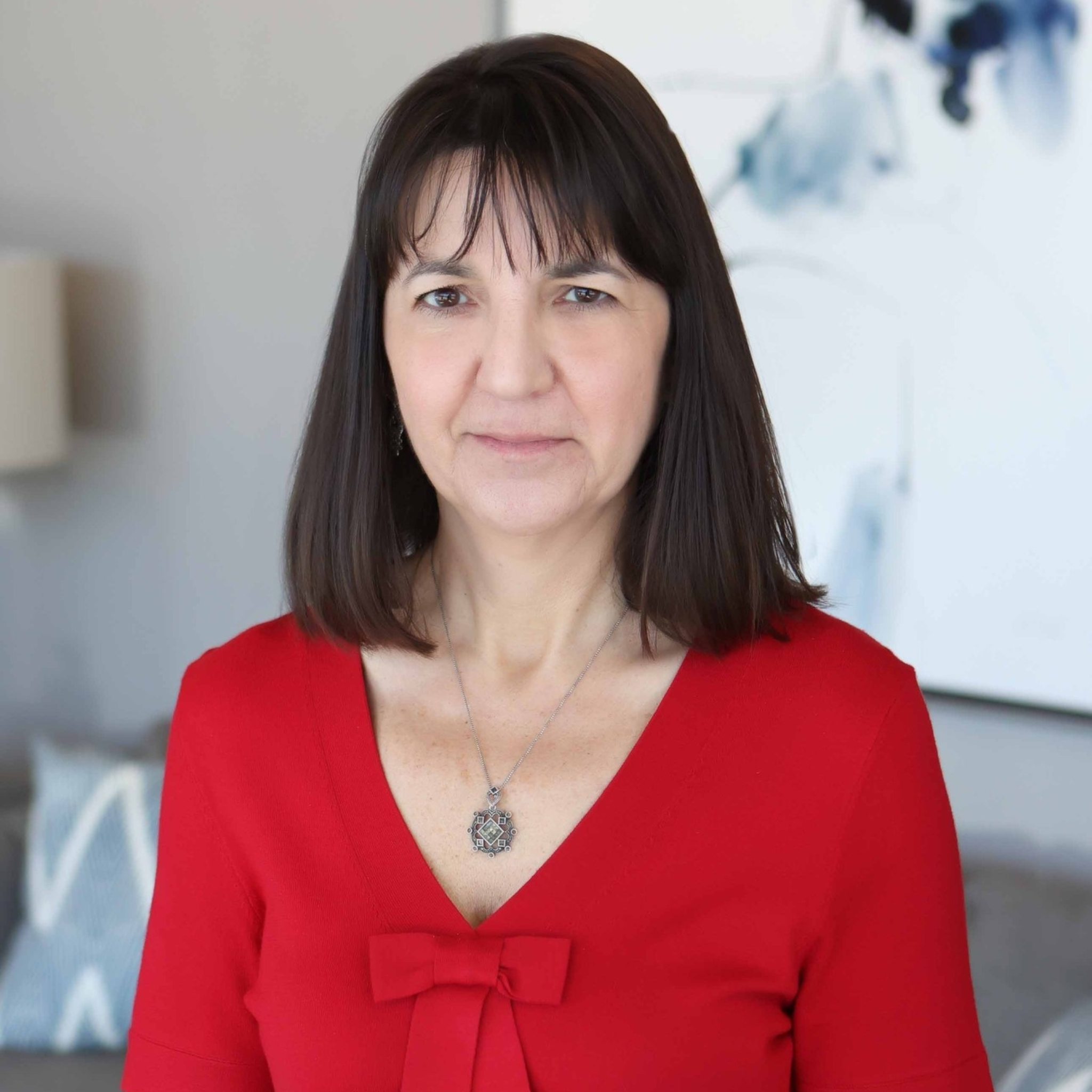 Close-up portrait of a young woman with long light brown hair wearing a denim jacket, smiling at the camera indoors.
