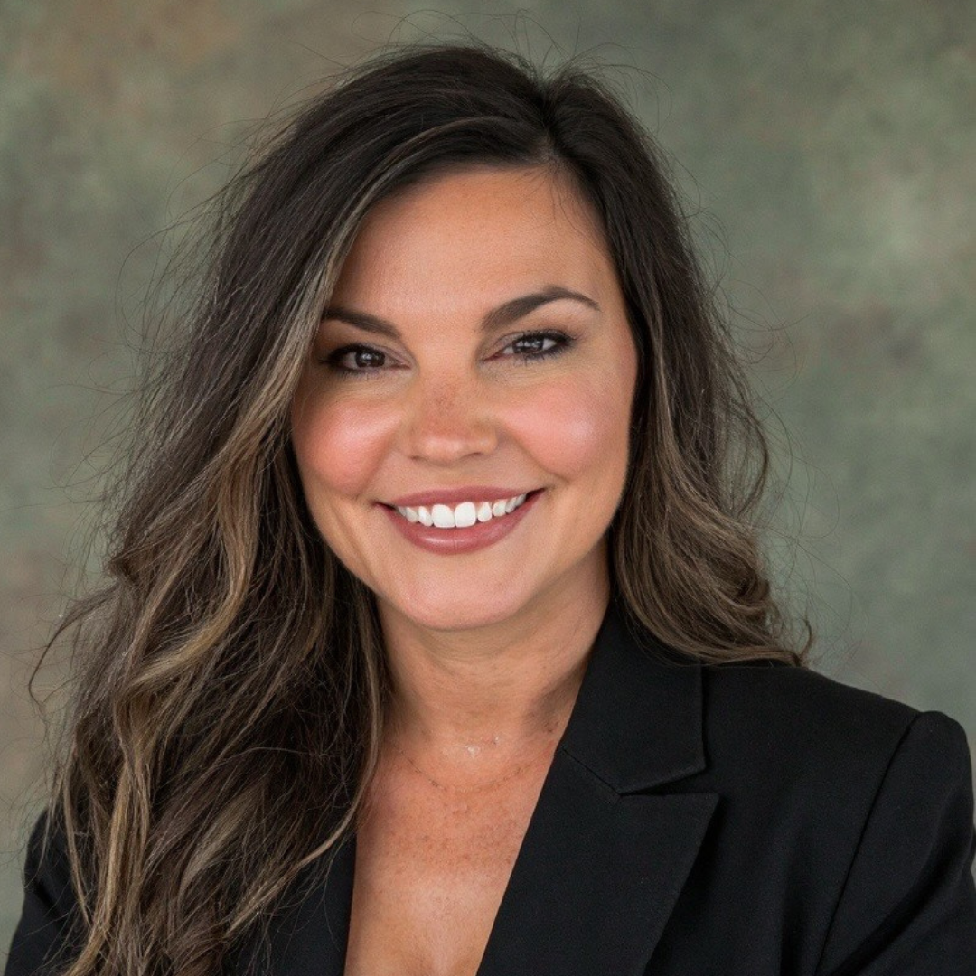 Smiling young woman with long brown hair wearing a green dress standing against a brick wall background