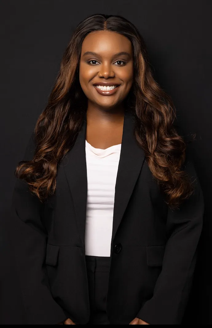 Portrait of a confident African American woman smiling in professional black blazer and white top against a dark background.