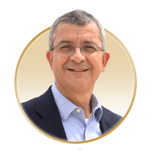 Portrait of a woman with curly blonde hair wearing a white blouse with red cherry patterns, smiling against a neutral gray background.