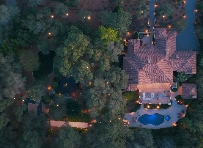 Twilight aerial of 5161 Greyson Creek Drive — landscape lighting through oak canopy, El Dorado Hills