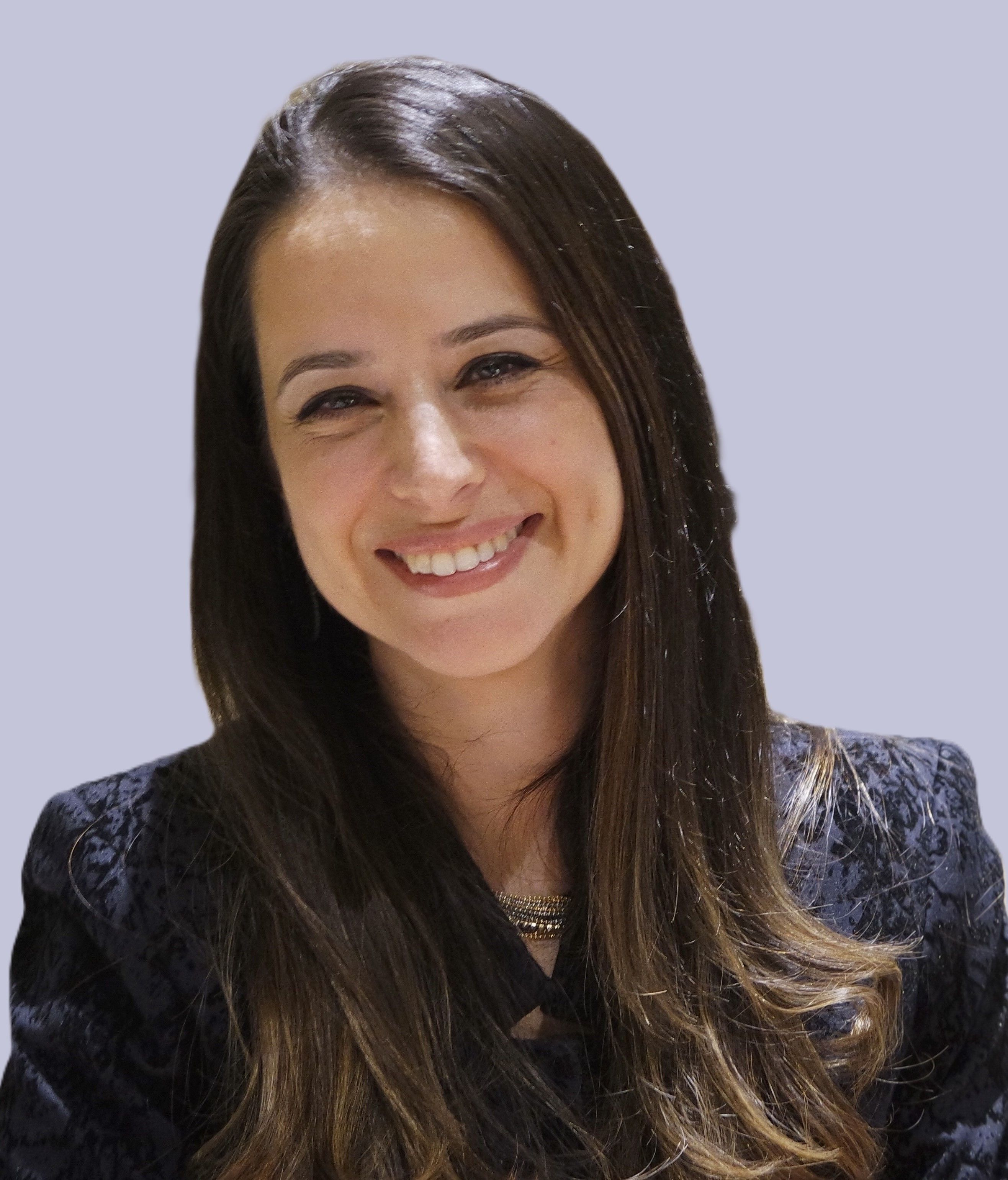 Smiling woman with long brown hair wearing a black patterned blazer and gold jewelry, posing against a light blue background.