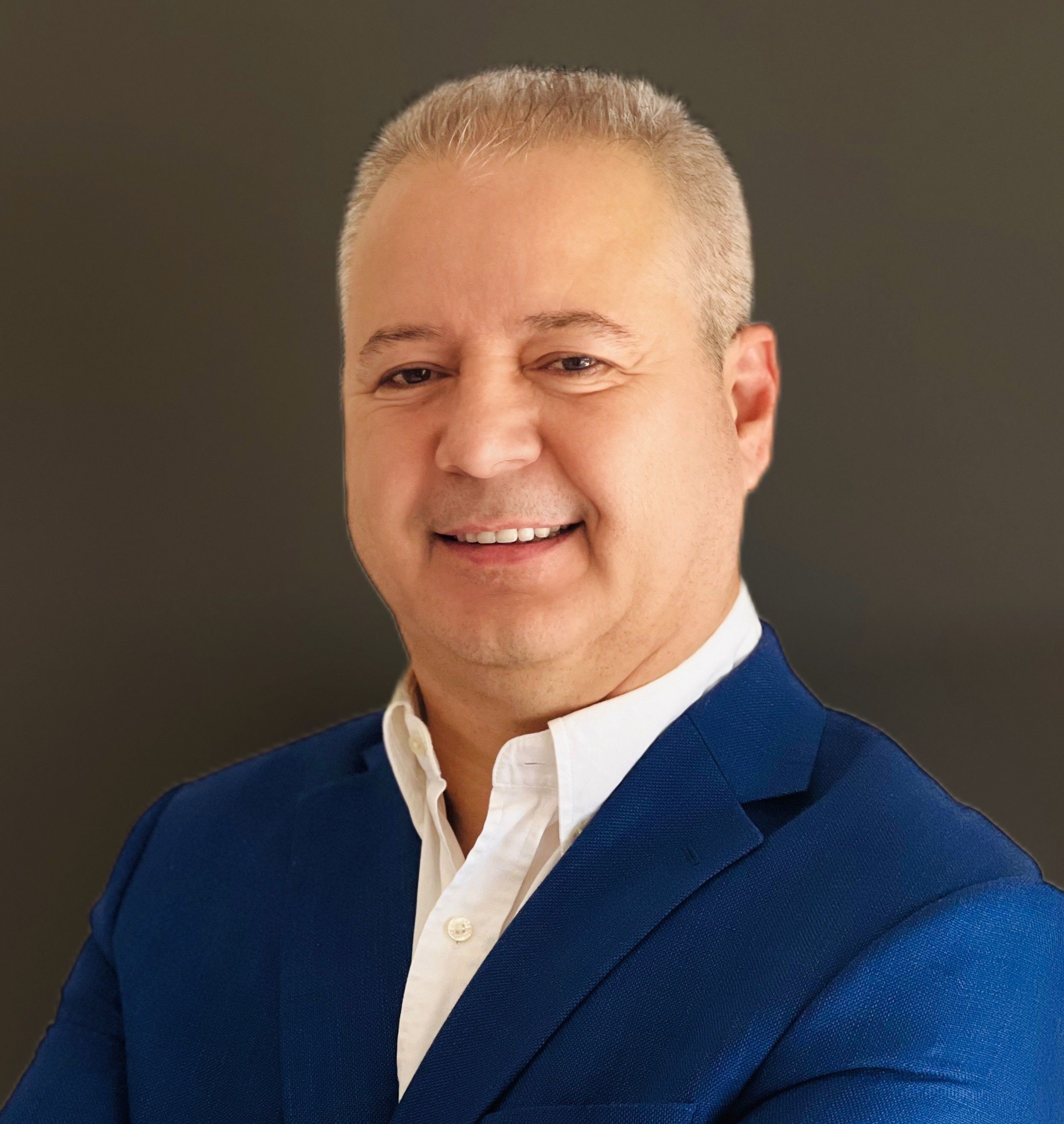 Professional headshot of a middle-aged man with short, light-colored hair, wearing a blue blazer and a white dress shirt, smiling against a neutral background.