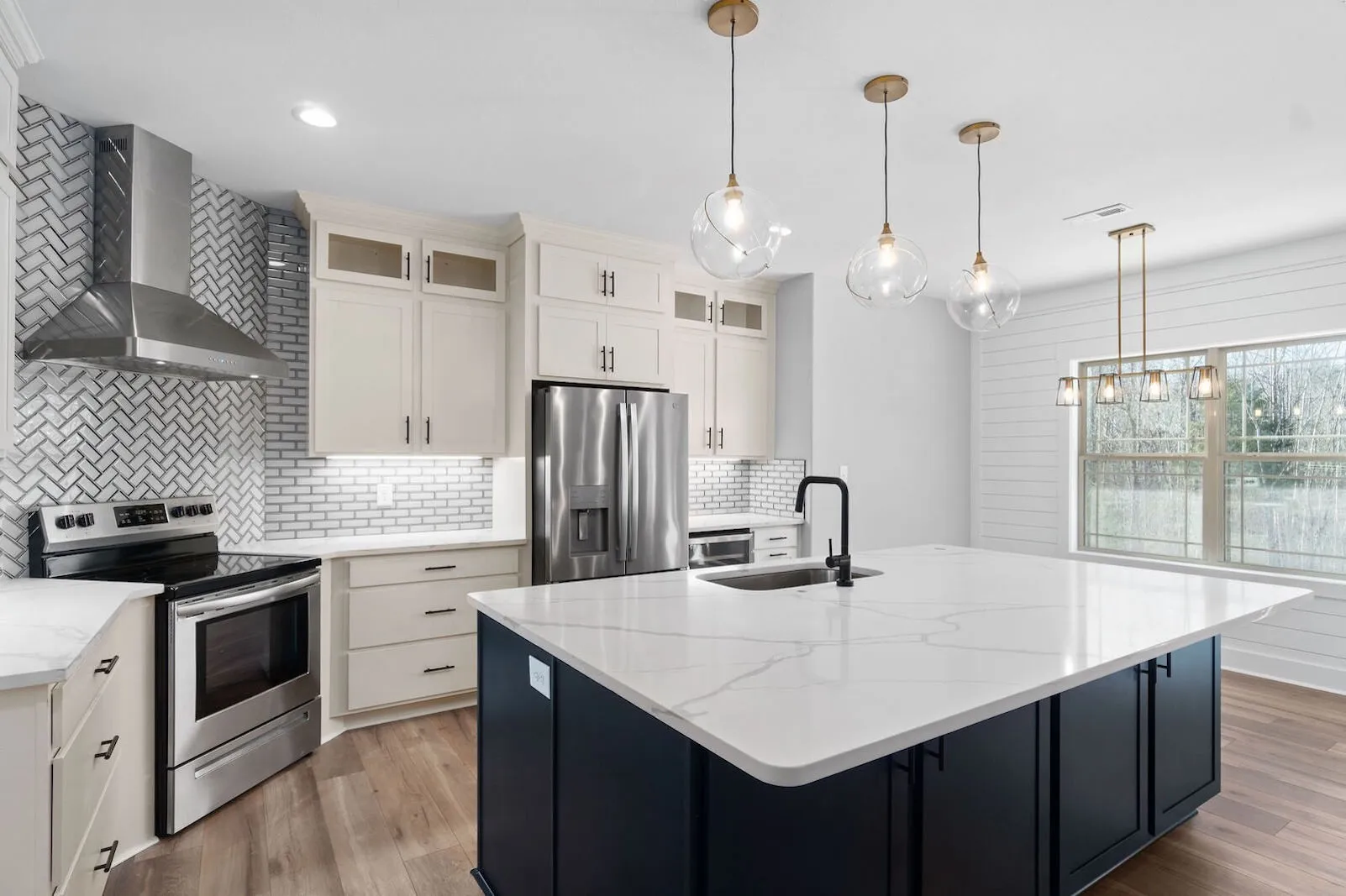 Modern kitchen with white cabinetry, stainless steel appliances, a large marble island, black accents, and contemporary lighting fixtures
