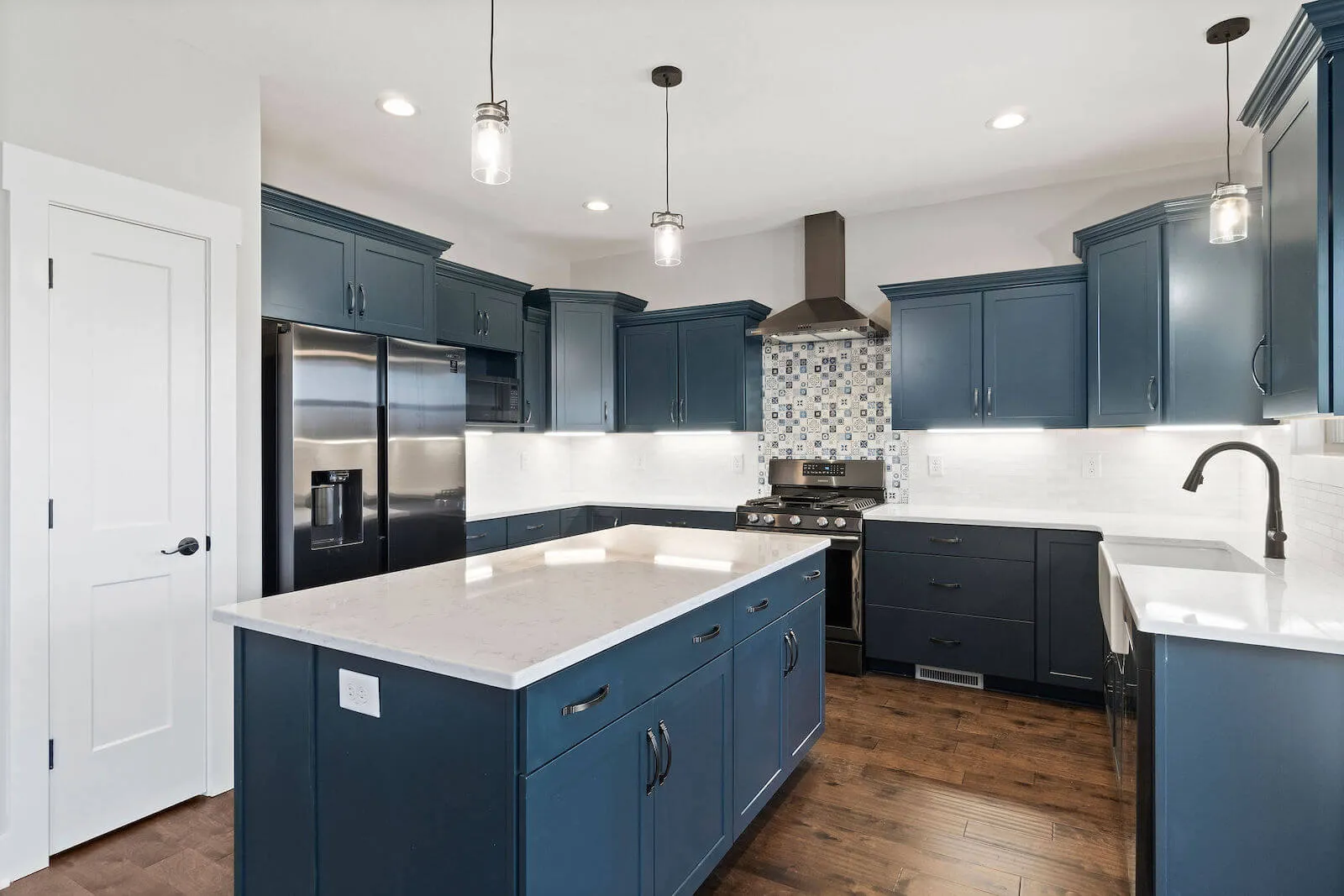 Modern kitchen with blue cabinets, stainless steel appliances, white countertops, and a wooden floor.