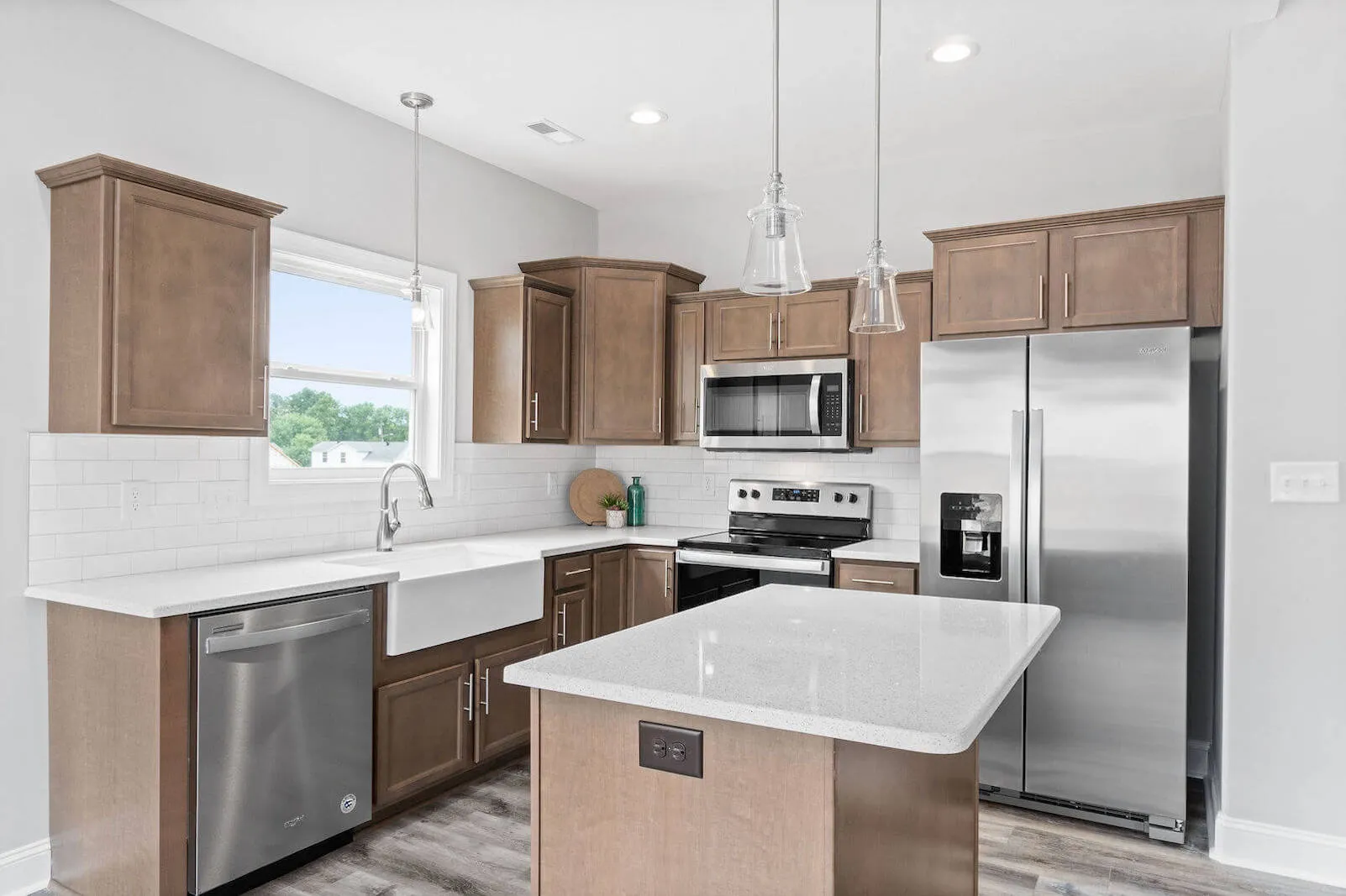 Modern kitchen with wooden cabinets, stainless steel appliances, white countertops, and a farmhouse sink, natural light coming through a window.