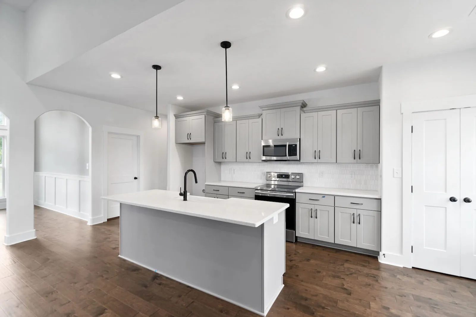 Modern white kitchen with gray cabinets, stainless steel appliances, island with black faucet, and hardwood floors.