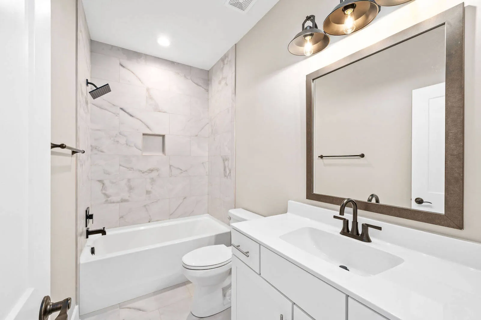 Modern bathroom with white vanity, large mirror, black fixtures, and a bathtub with marble tiles and a built-in niche for toiletries