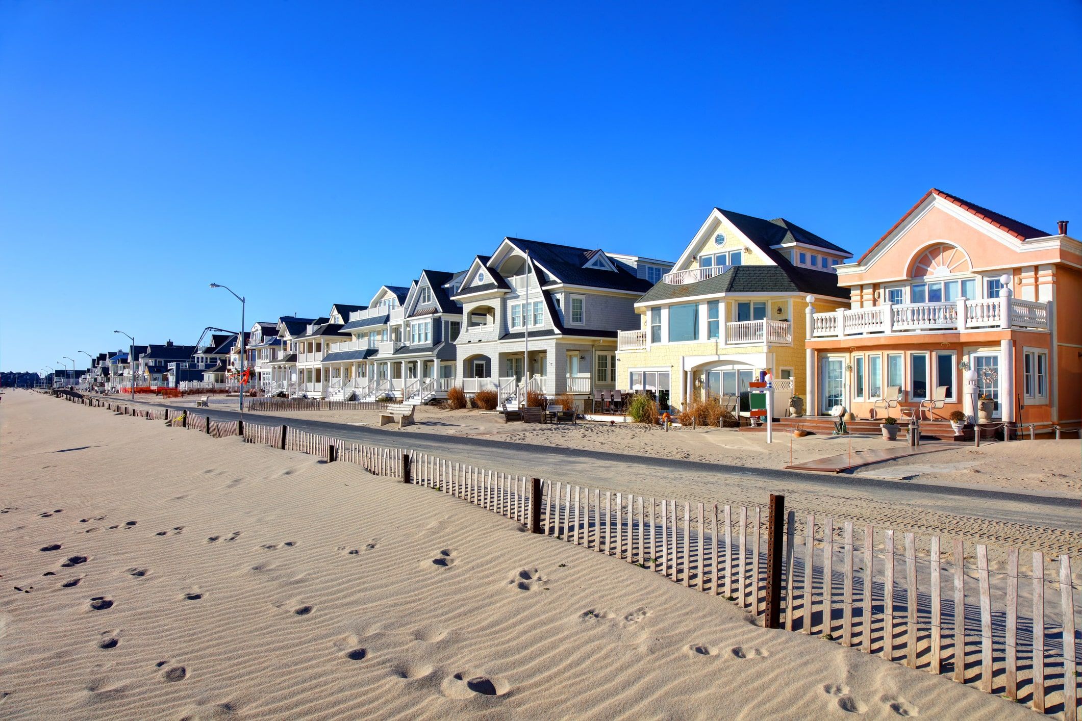 Colorful beach houses along a sandy shoreline with a clear blue sky and footprints in the sand.