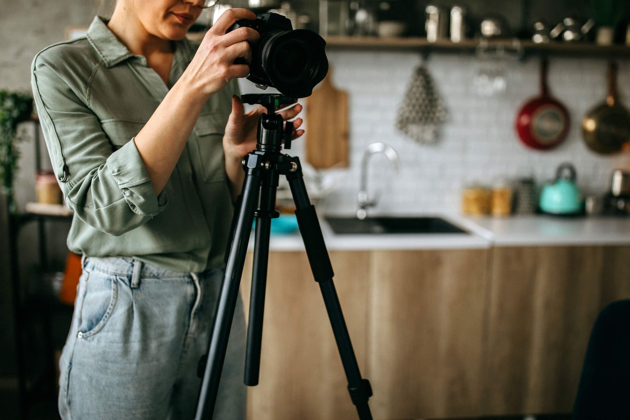 Woman adjusting professional camera on tripod in a modern kitchen setting.