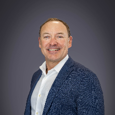 Smiling woman with wavy blonde hair wearing a black and white patterned top against a neutral background