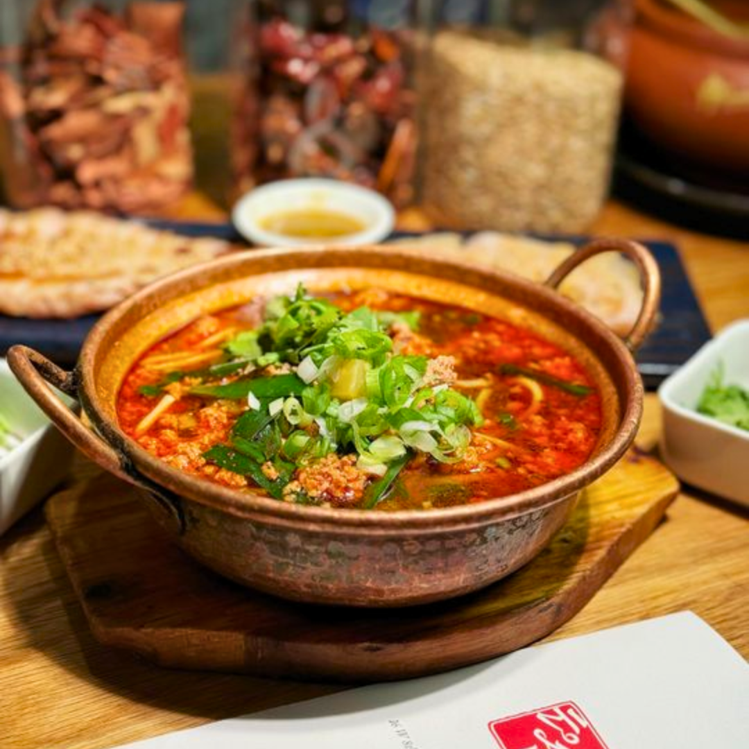 Plate with hamburger, French fries, lettuce, tomato, and onion sandwich with side of French fries on a white table, accompanied by a glass of dark soda, ketchup, and salt and pepper shakers.