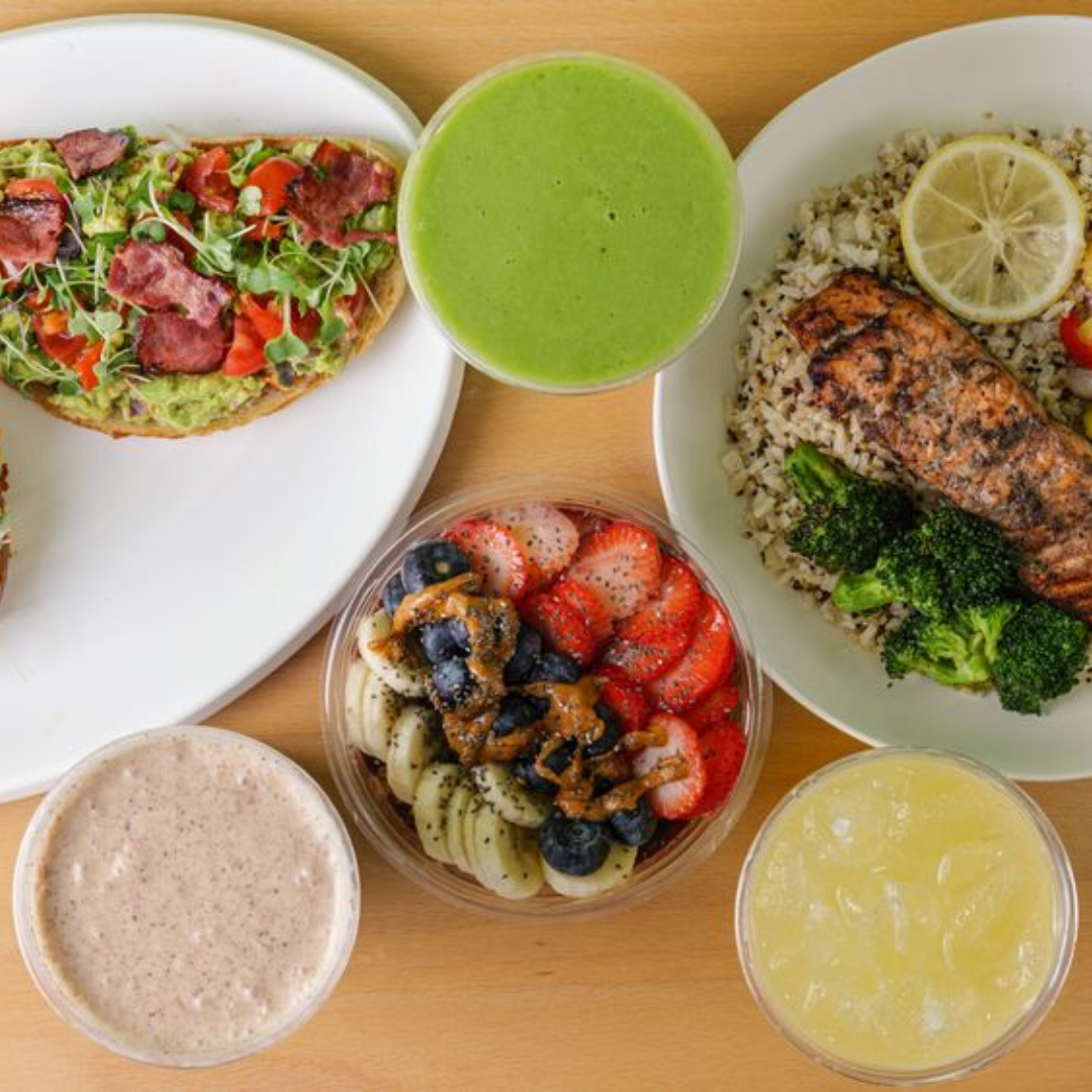 Plate with hamburger, French fries, lettuce, tomato, and onion sandwich with side of French fries on a white table, accompanied by a glass of dark soda, ketchup, and salt and pepper shakers.