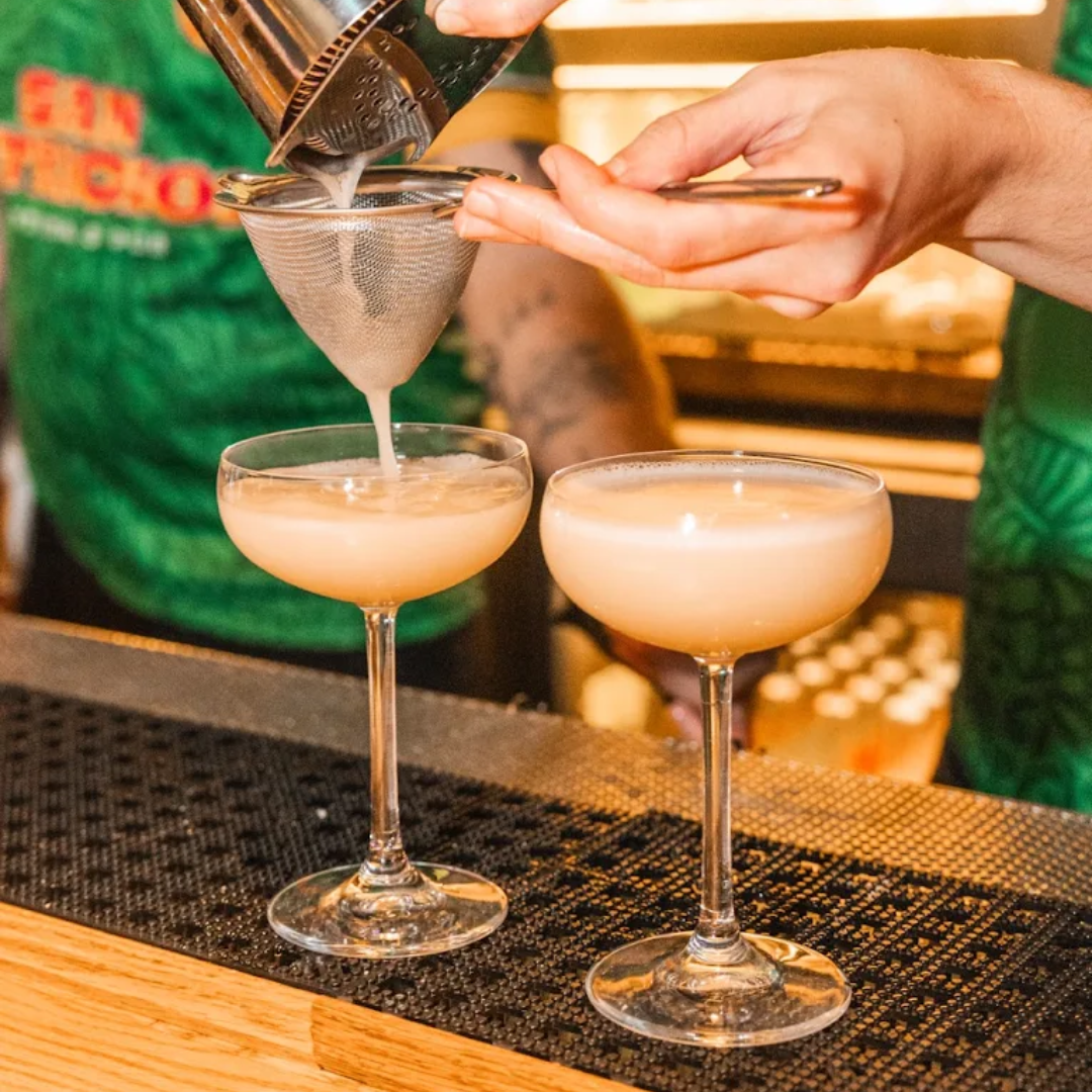 Plate with hamburger, French fries, lettuce, tomato, and onion sandwich with side of French fries on a white table, accompanied by a glass of dark soda, ketchup, and salt and pepper shakers.