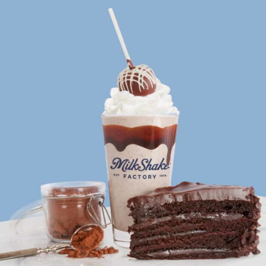 Plate with hamburger, French fries, lettuce, tomato, and onion sandwich with side of French fries on a white table, accompanied by a glass of dark soda, ketchup, and salt and pepper shakers.