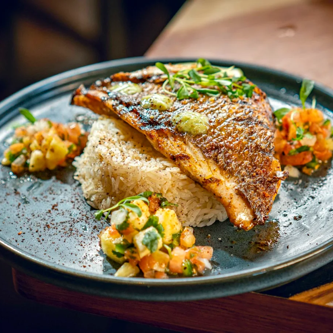 Grilled salmon fillet with garlic herb butter, served with white rice and vegetable salsa on a dark ceramic plate.