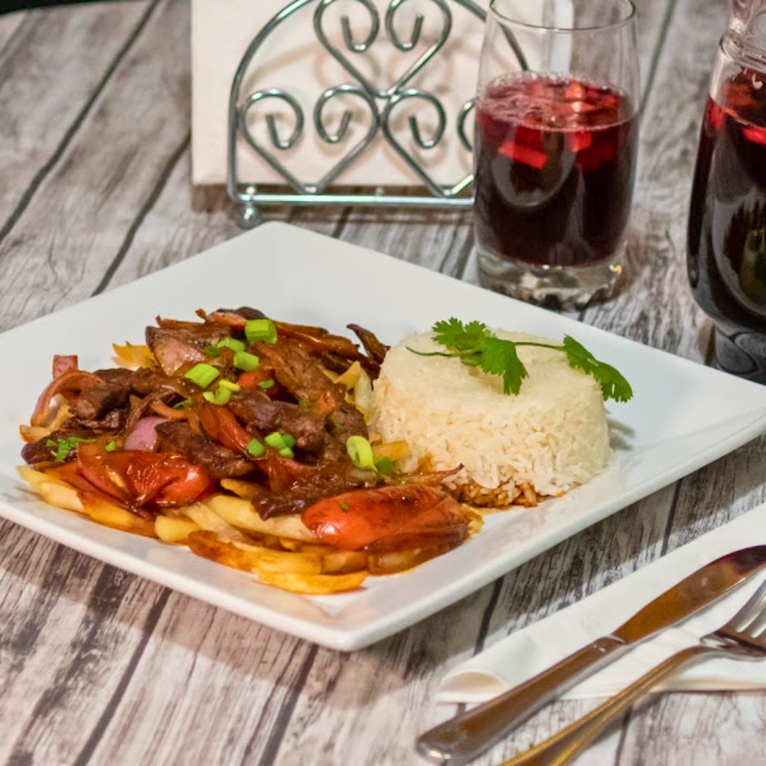 Plate of beef stew with vegetables, served with a side of white rice garnished with cilantro, accompanied by glasses of red wine on a rustic wooden table.