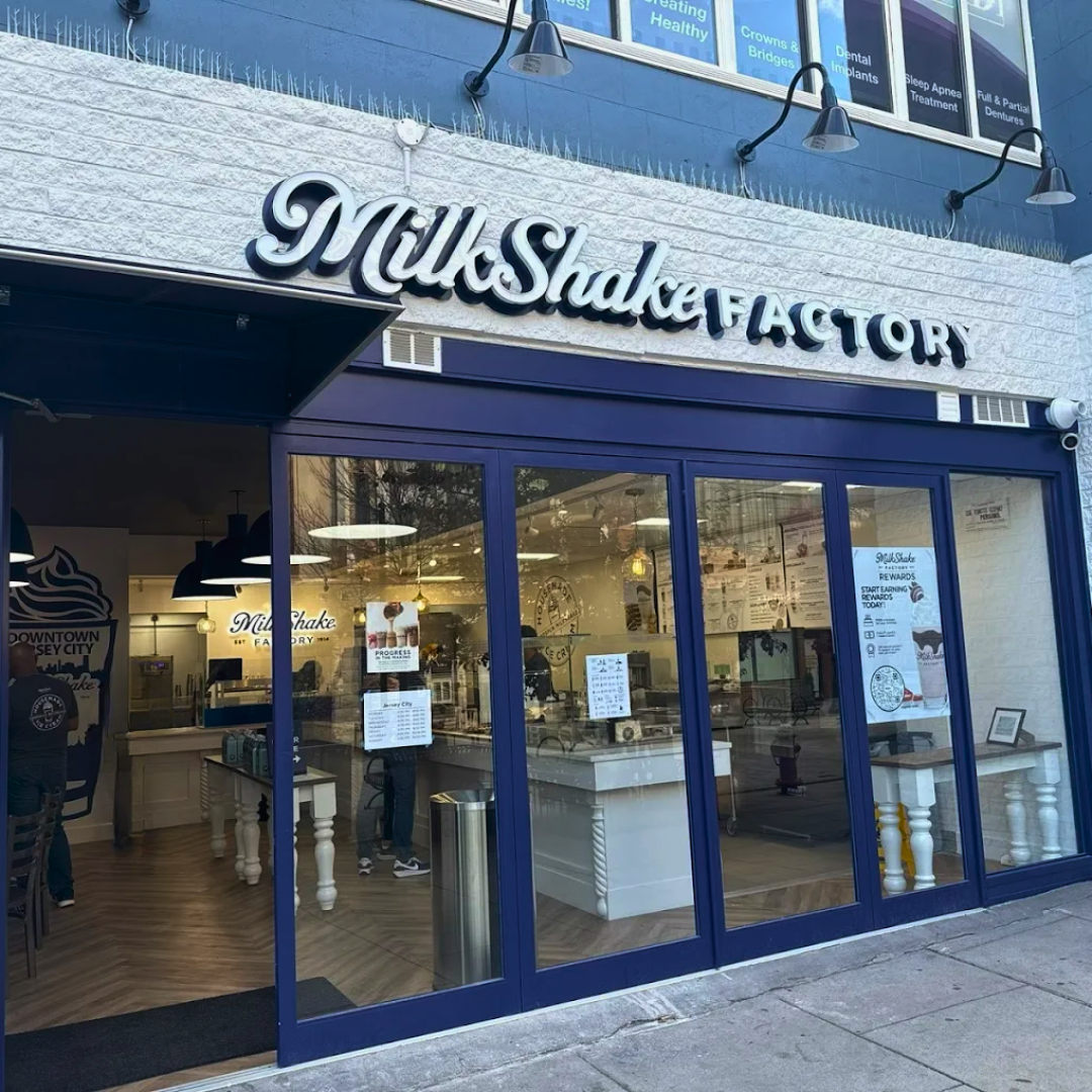 Exterior view of a Milkshake Factory storefront with a glass entrance, white brick facade, and signage displaying 