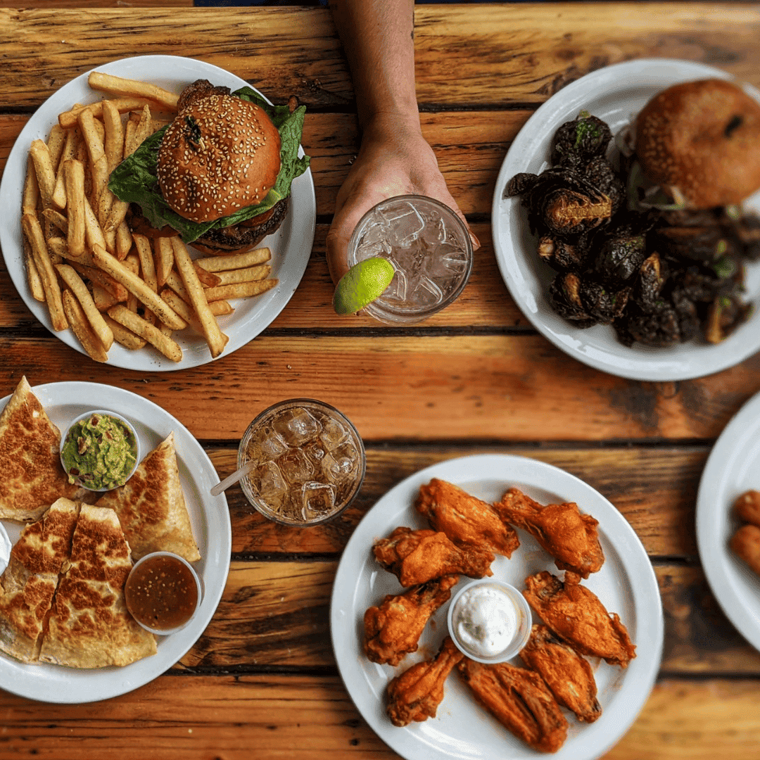 Plate with hamburger, French fries, lettuce, tomato, and onion sandwich with side of French fries on a white table, accompanied by a glass of dark soda, ketchup, and salt and pepper shakers.