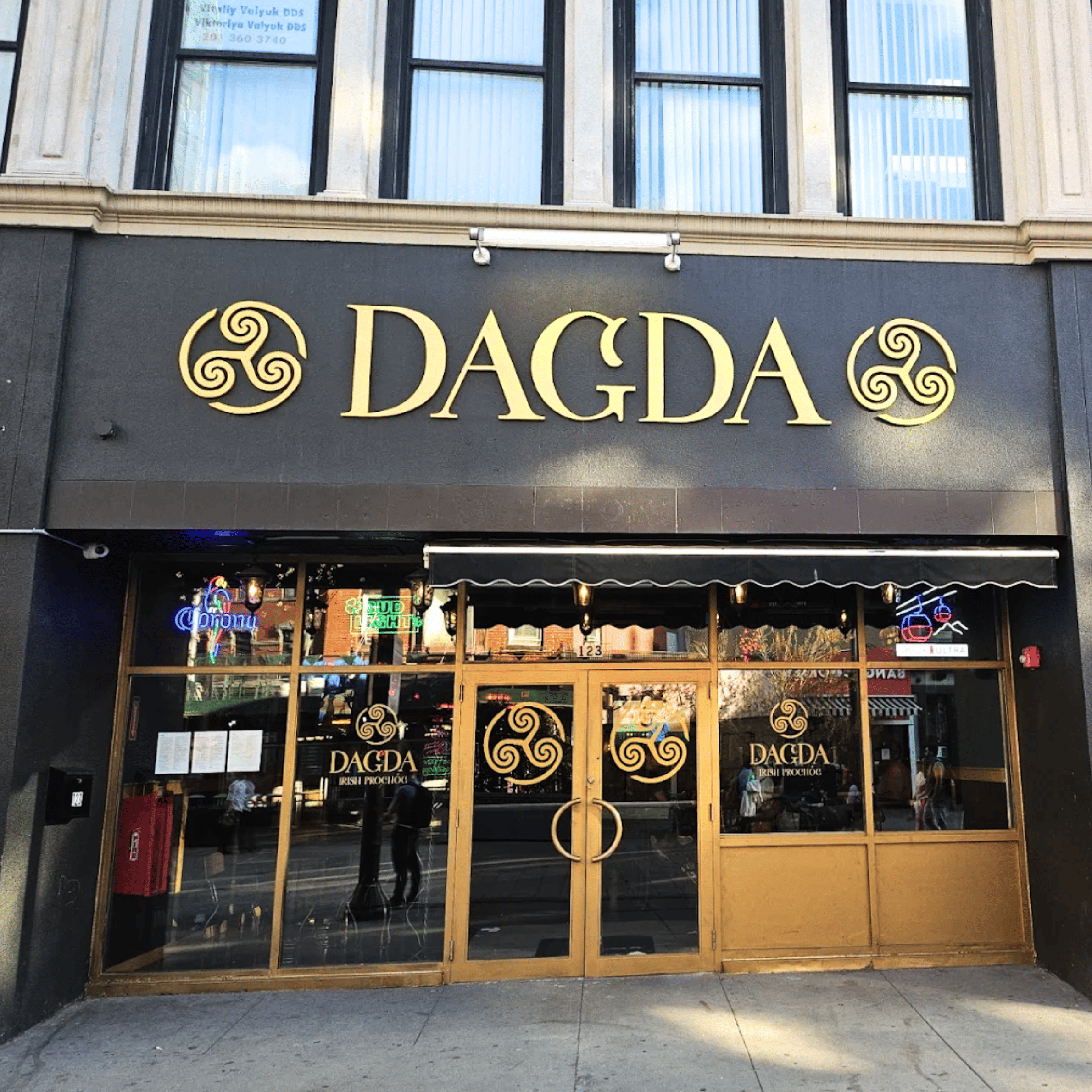 Exterior view of a corner pizzeria restaurant with large glass windows, brick upper walls, and potted plants on the window ledge, featuring signs for salads, pasta, and pizza.