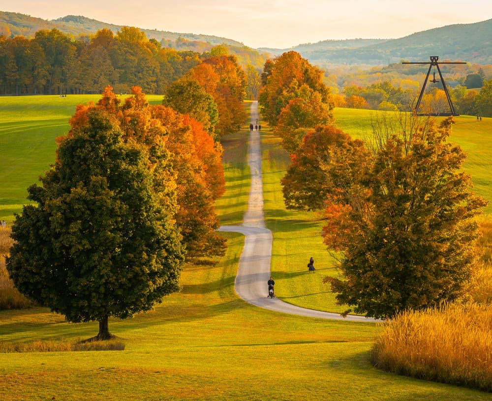 Scenic autumn landscape at a golf course with vibrant fall foliage, a winding path, and people walking and biking amidst colorful trees and rolling hills