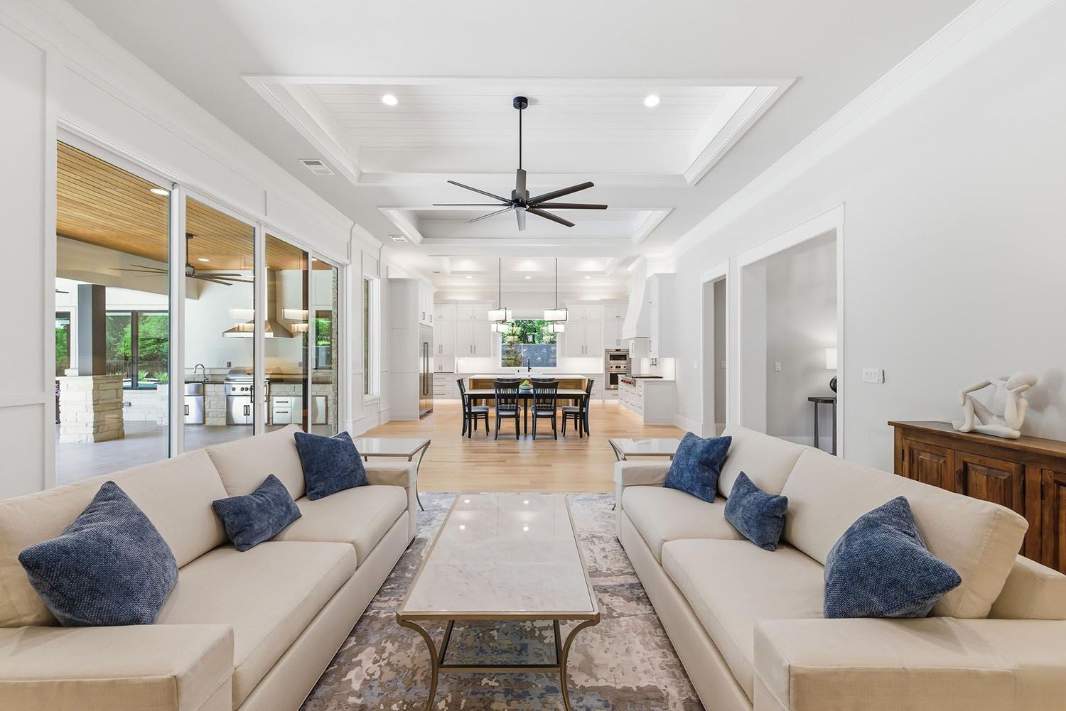 Modern farmhouse kitchen with white cabinetry, a large island with granite countertop, and a dining area with sliding glass doors opening to an outdoor patio.