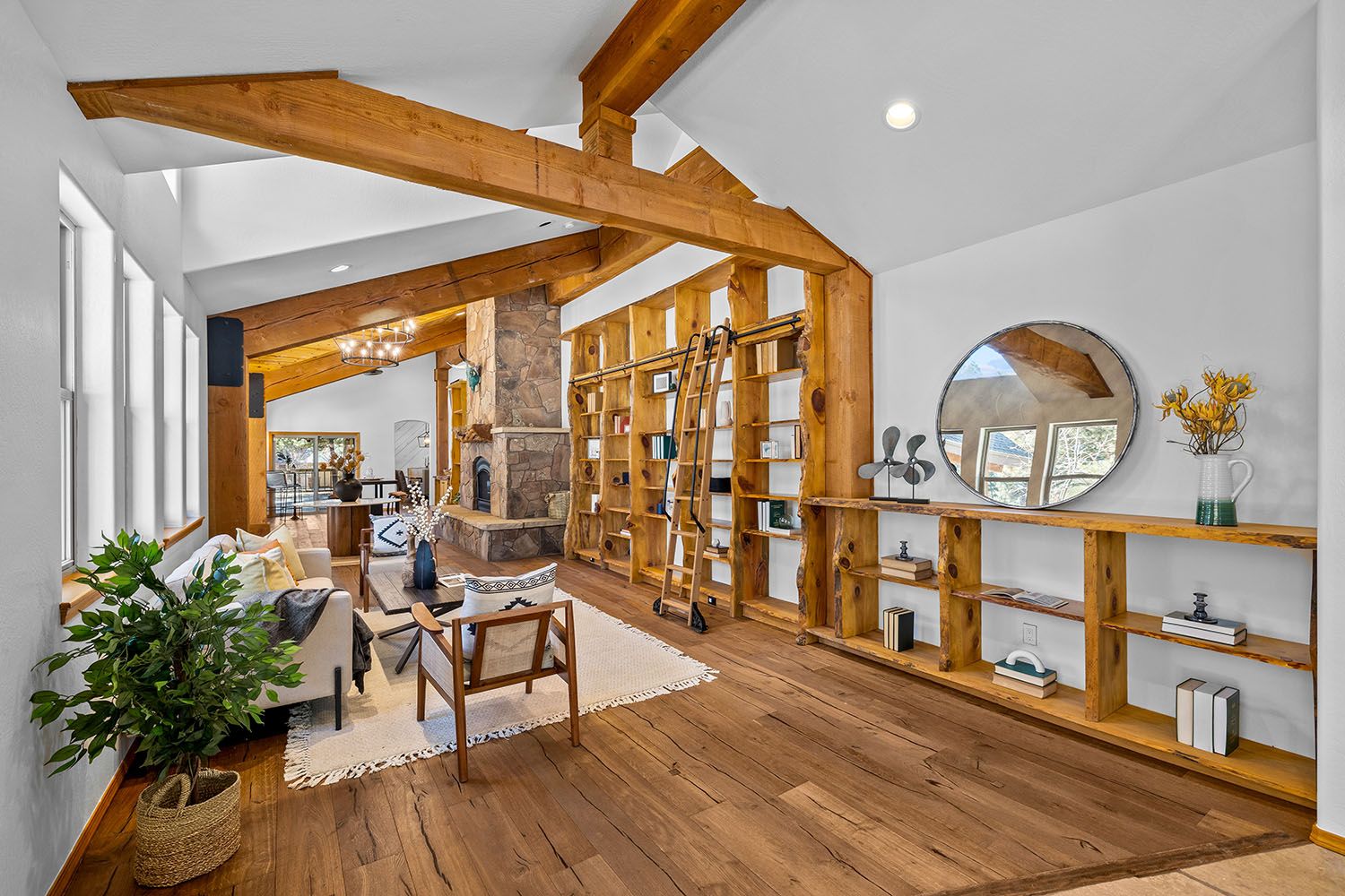 Rustic dining room with wooden floors, stone fireplace, cozy windows, and natural light, connecting to the kitchen.