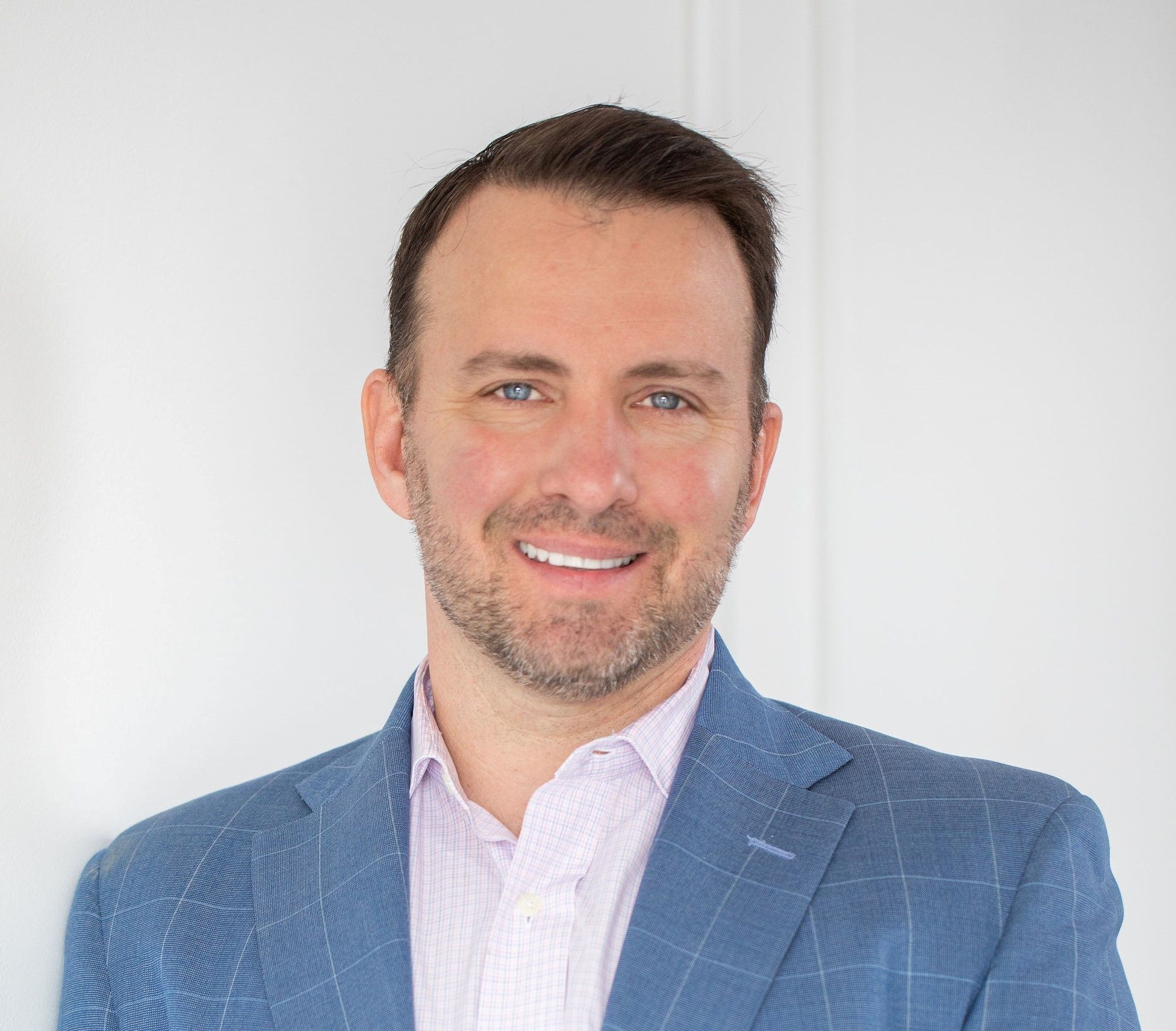 Smiling young man in a blue checked blazer and white shirt, professional headshot on white background