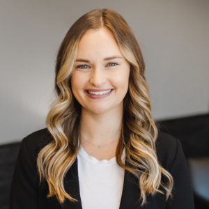 Smiling young woman with wavy blonde hair wearing a black blazer and white top, professional portrait