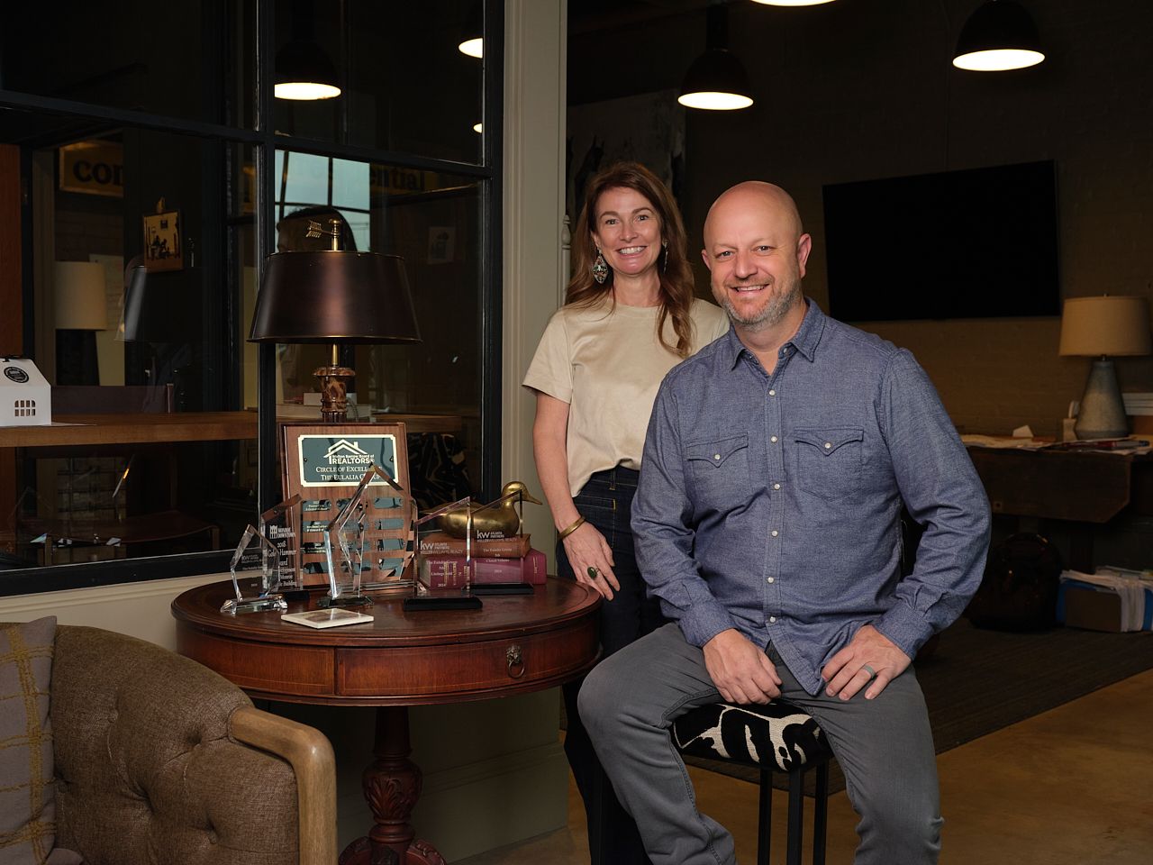 Group of two professionals smiling indoors, casual and business attire, in a modern office or conference setting.