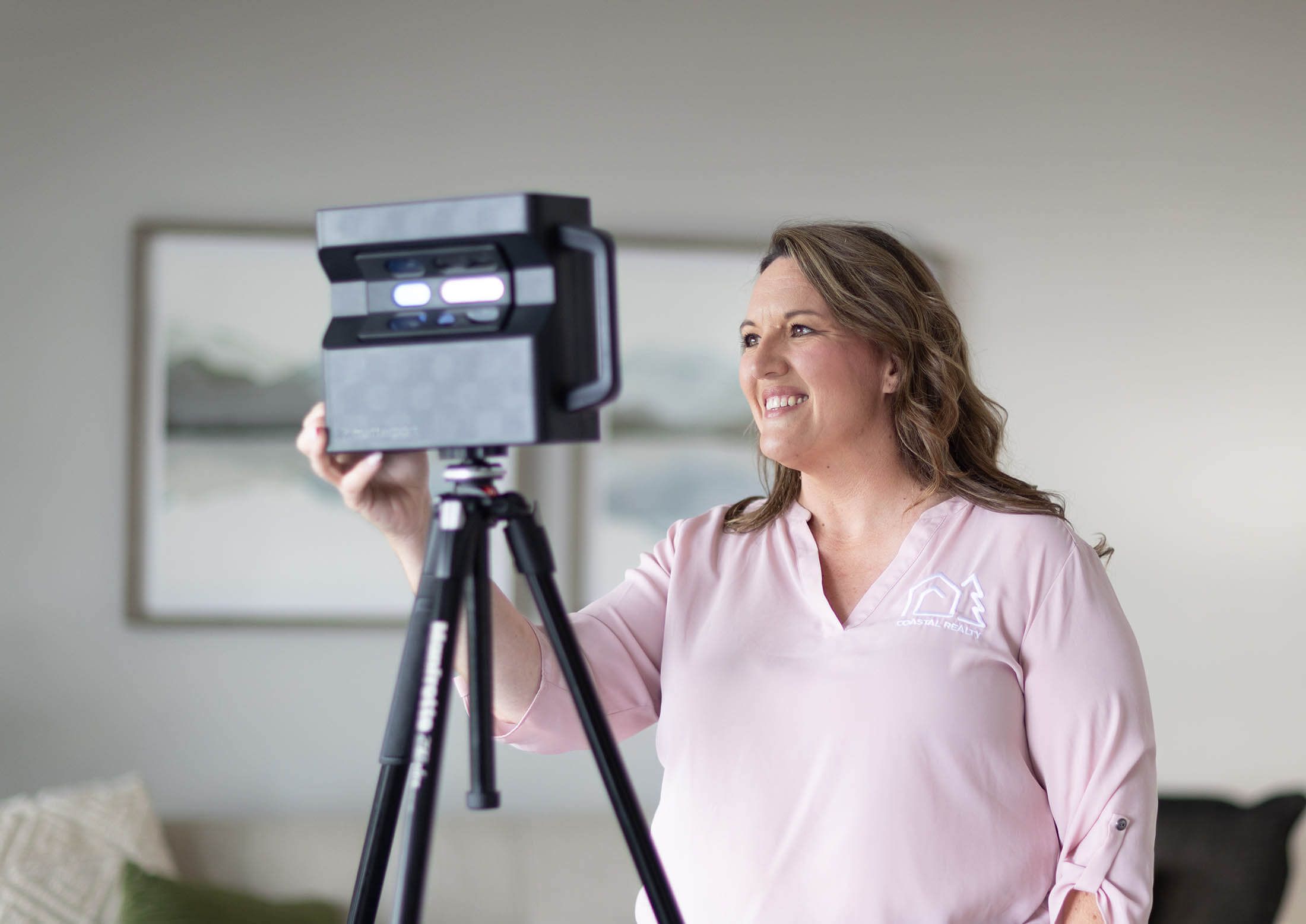 Two people smiling and looking at a phone while operating a digital camera on a tripod during sunset with a city skyline in the background