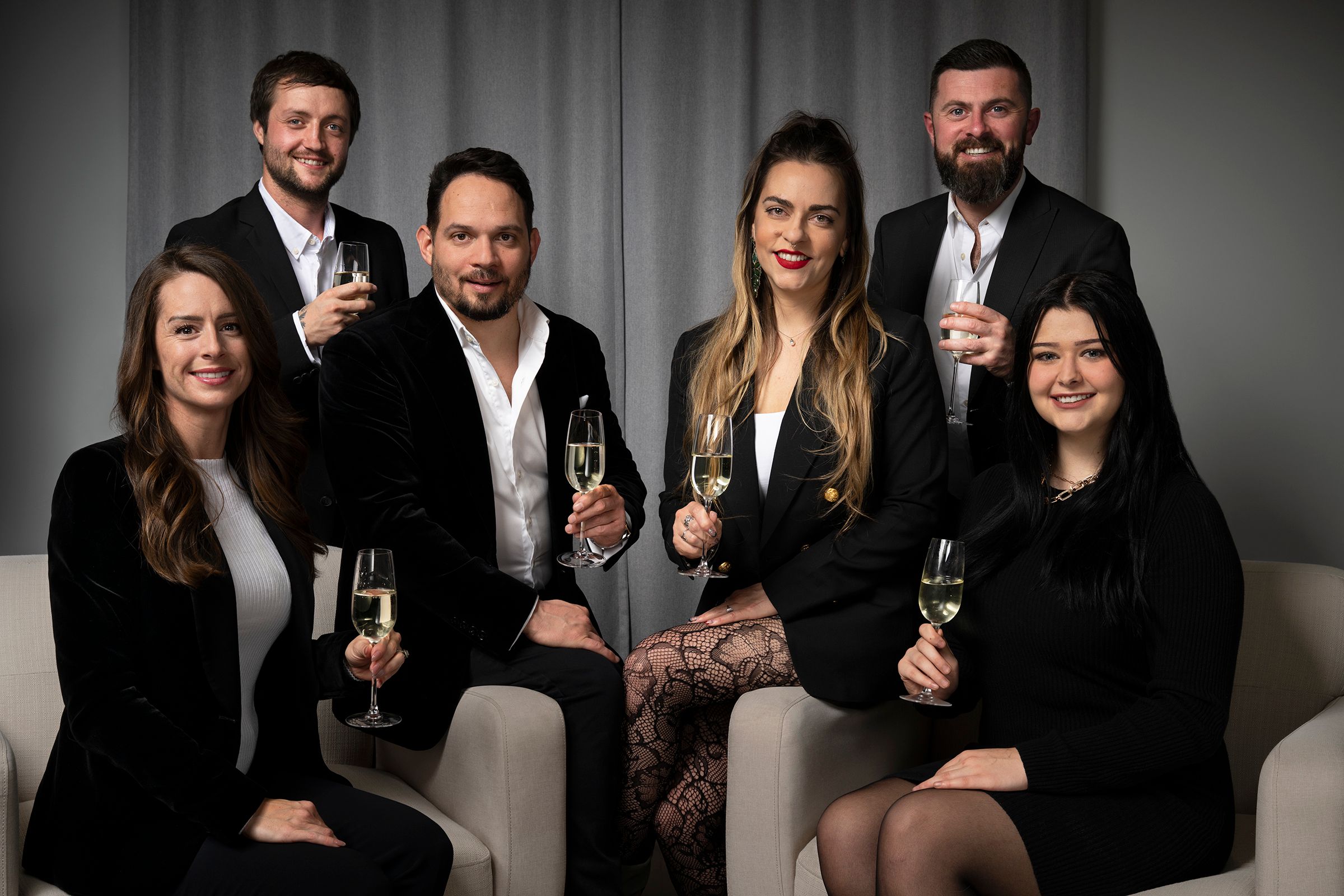 Group of four diverse business professionals in formal attire standing together in modern office hallway with large plant in background