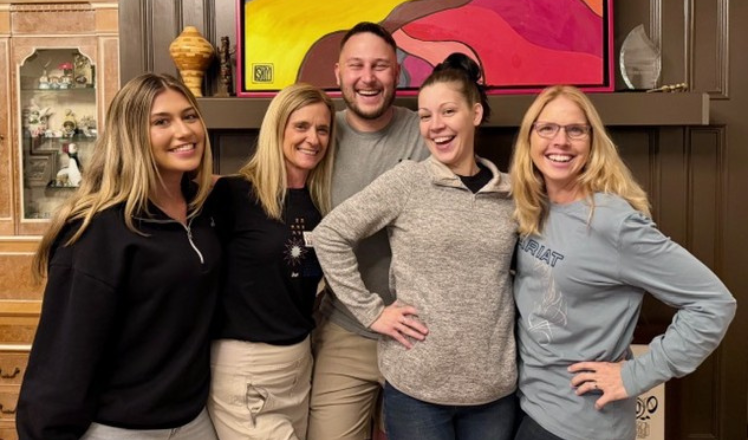 Group of four diverse friends smiling outdoors in a park during daytime, enjoying friendship and nature.