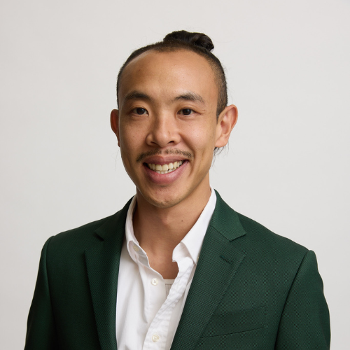Professional portrait of a smiling Asian man wearing a dark green suit jacket and white dress shirt against a plain white background