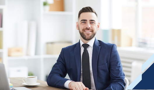 Confident young businessman in a navy suit smiling at the camera in a bright modern office setting