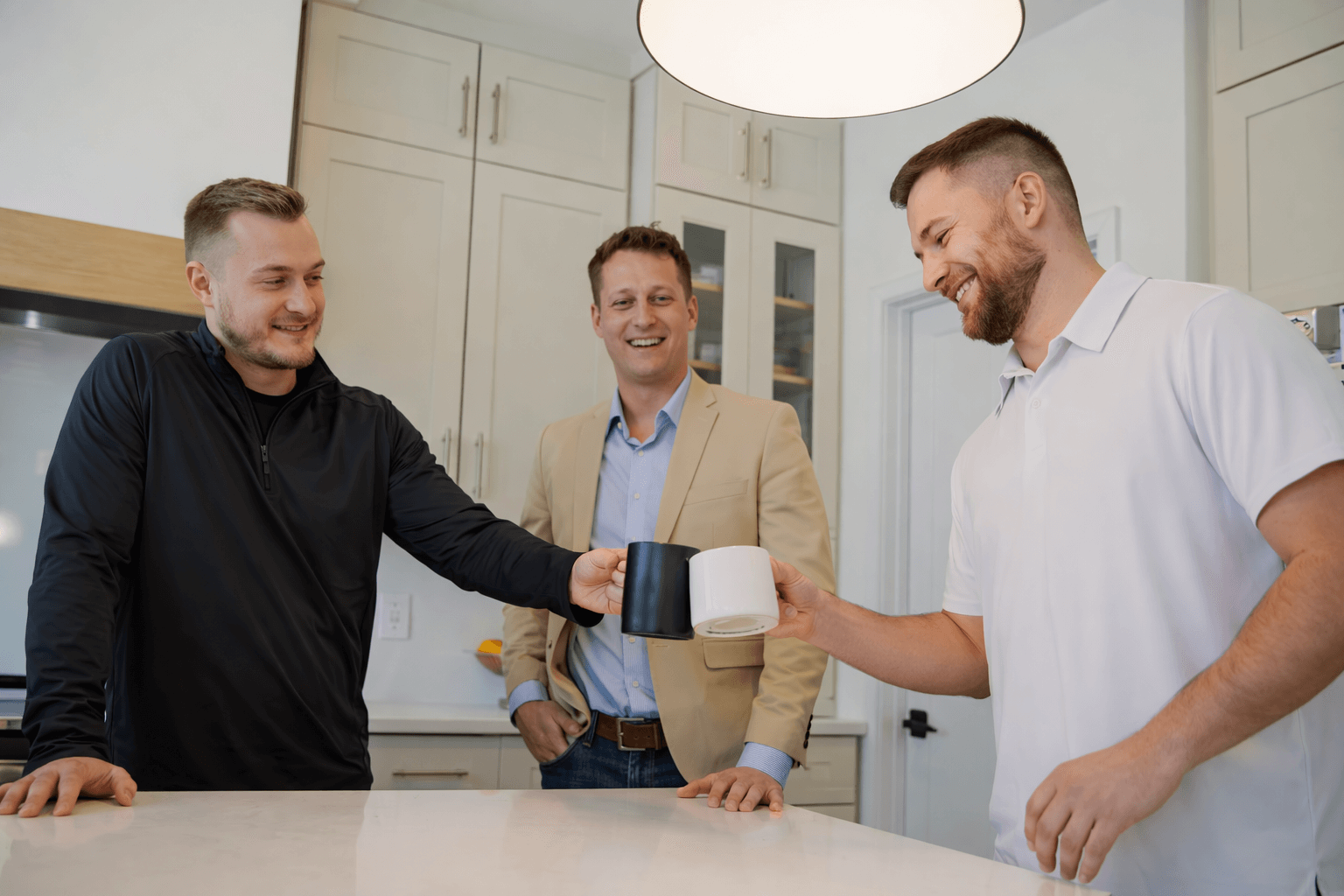 Three men exchanging mugs in a kitchen during a friendly meeting or celebration.