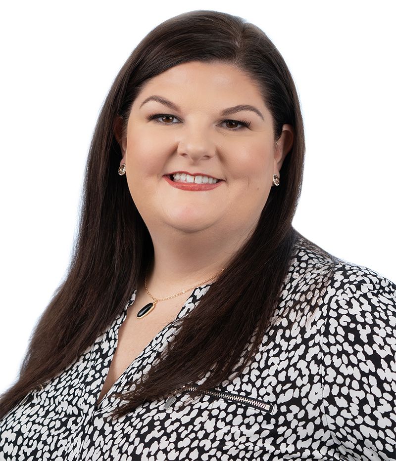 Professional woman smiling in a black and white patterned blouse with long dark hair, wearing jewelry, against a white background