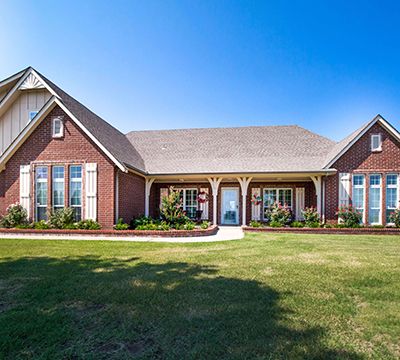 Spacious brick house with front porch, large windows, well-maintained lawn, and clear blue sky.