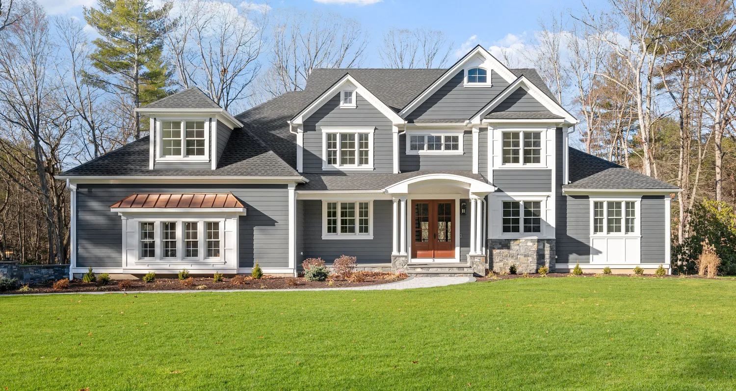 Newly under-construction house with a steep gray-shingled roof, dormer windows, and a partially built front porch on a clear day.