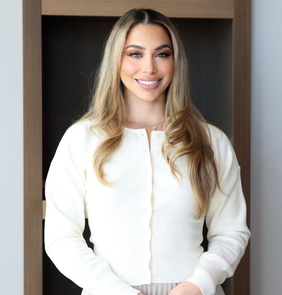 Professional woman with long, wavy blonde hair smiling in a business casual outfit indoors.