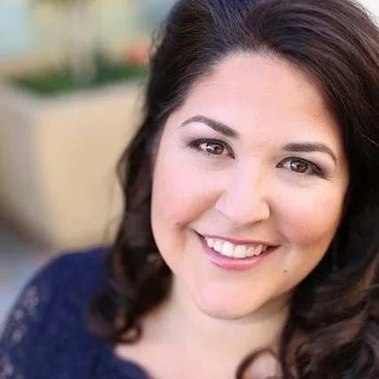 Close-up of smiling woman with dark brown hair, wearing a navy blue top, outdoor background