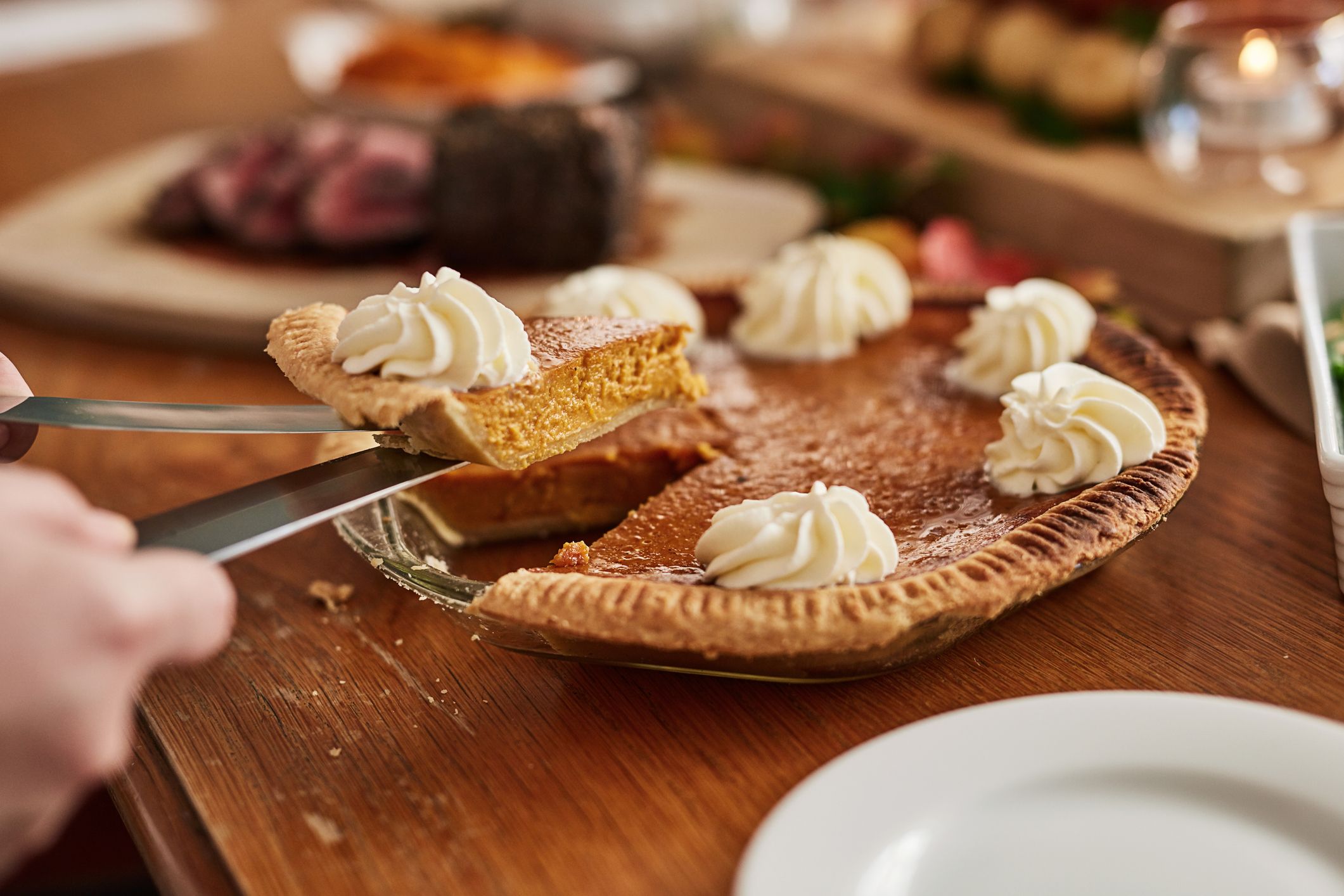 A slice of pumpkin pie with whipped cream being served at a holiday table