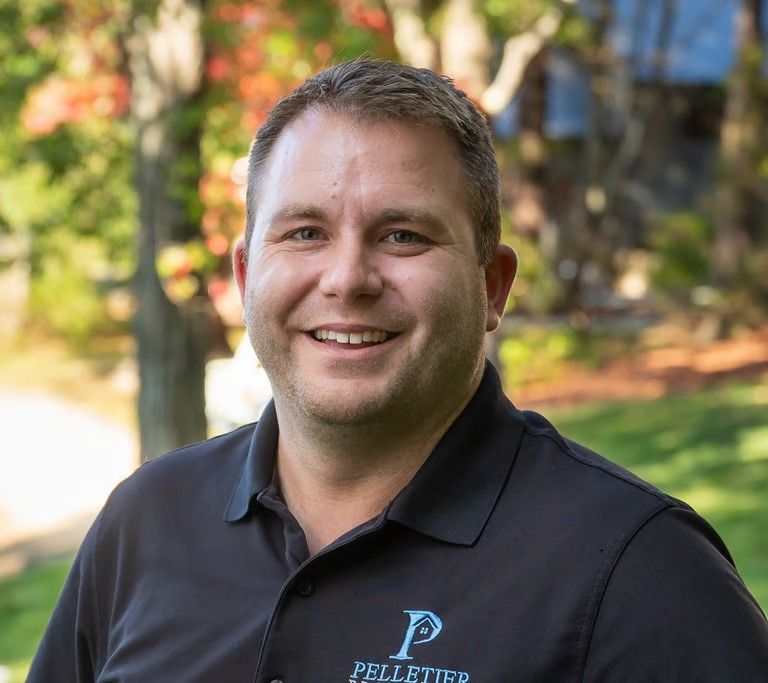Smiling elderly man with gray hair, glasses, pink shirt, and maroon sweater in a modern office setting.
