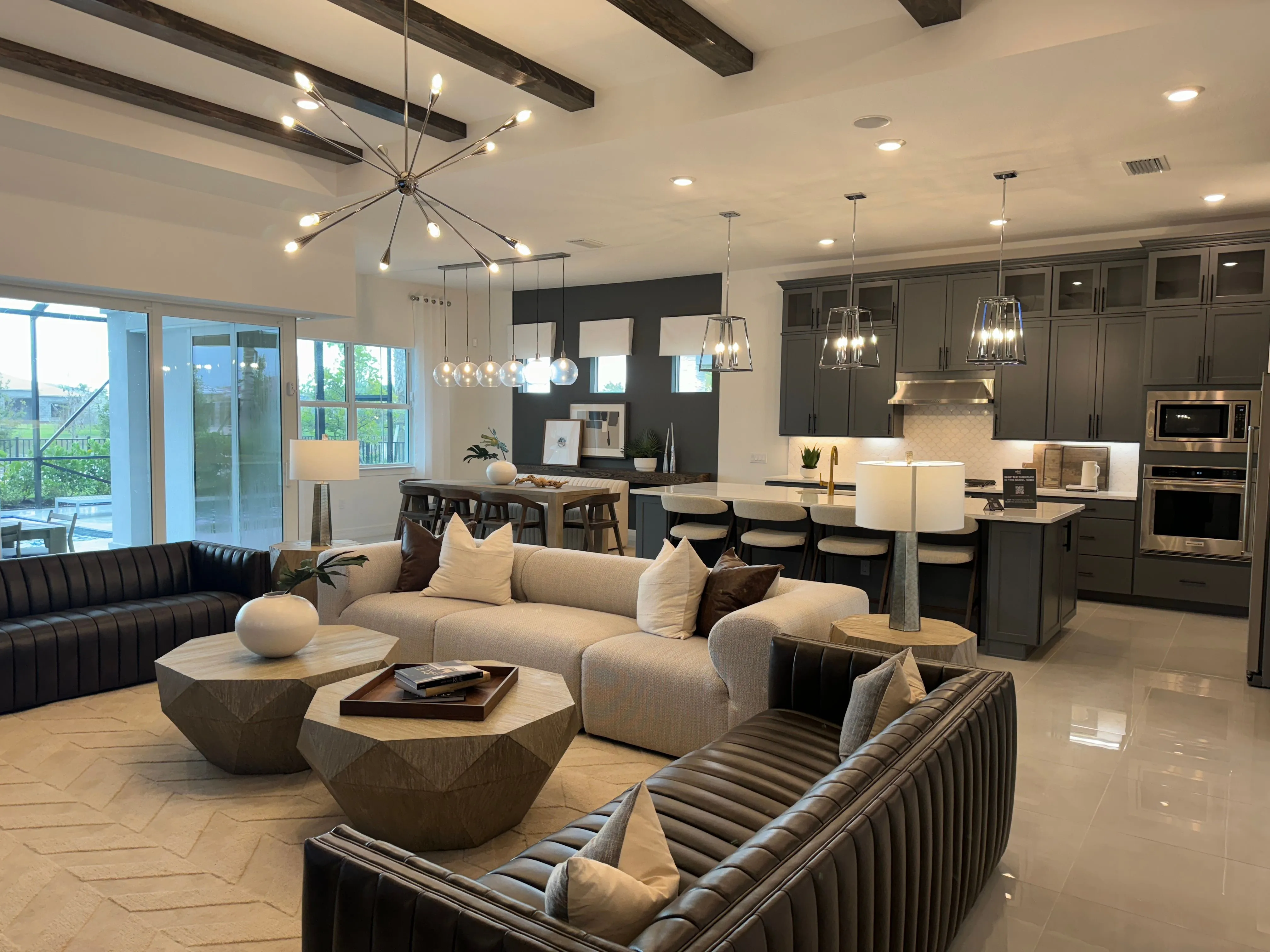 Open living room and kitchen with island seating, dark cabinetry and ceiling beams at Avondale at Avenir