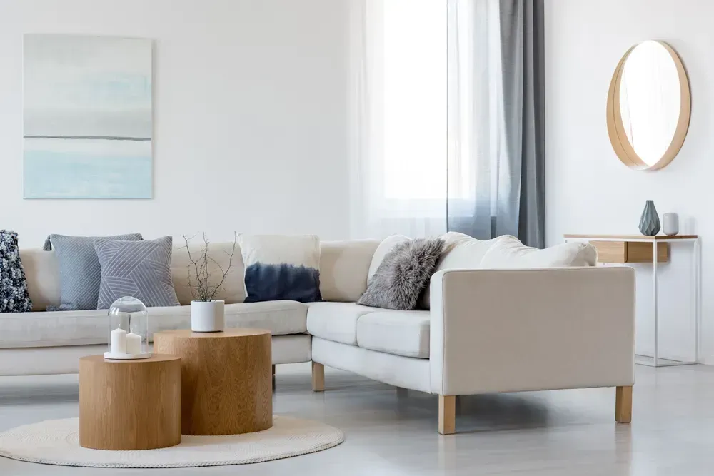 Bright living room with a white sectional sofa, round wood tables and wall mirror