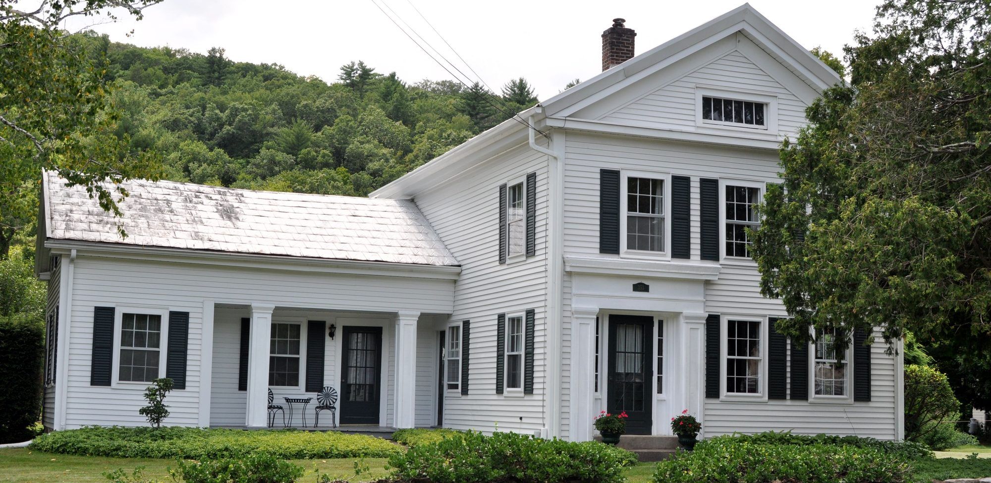 A white Greek Revival farmhouse with black shutters and a columned porch on a Fairfield County road