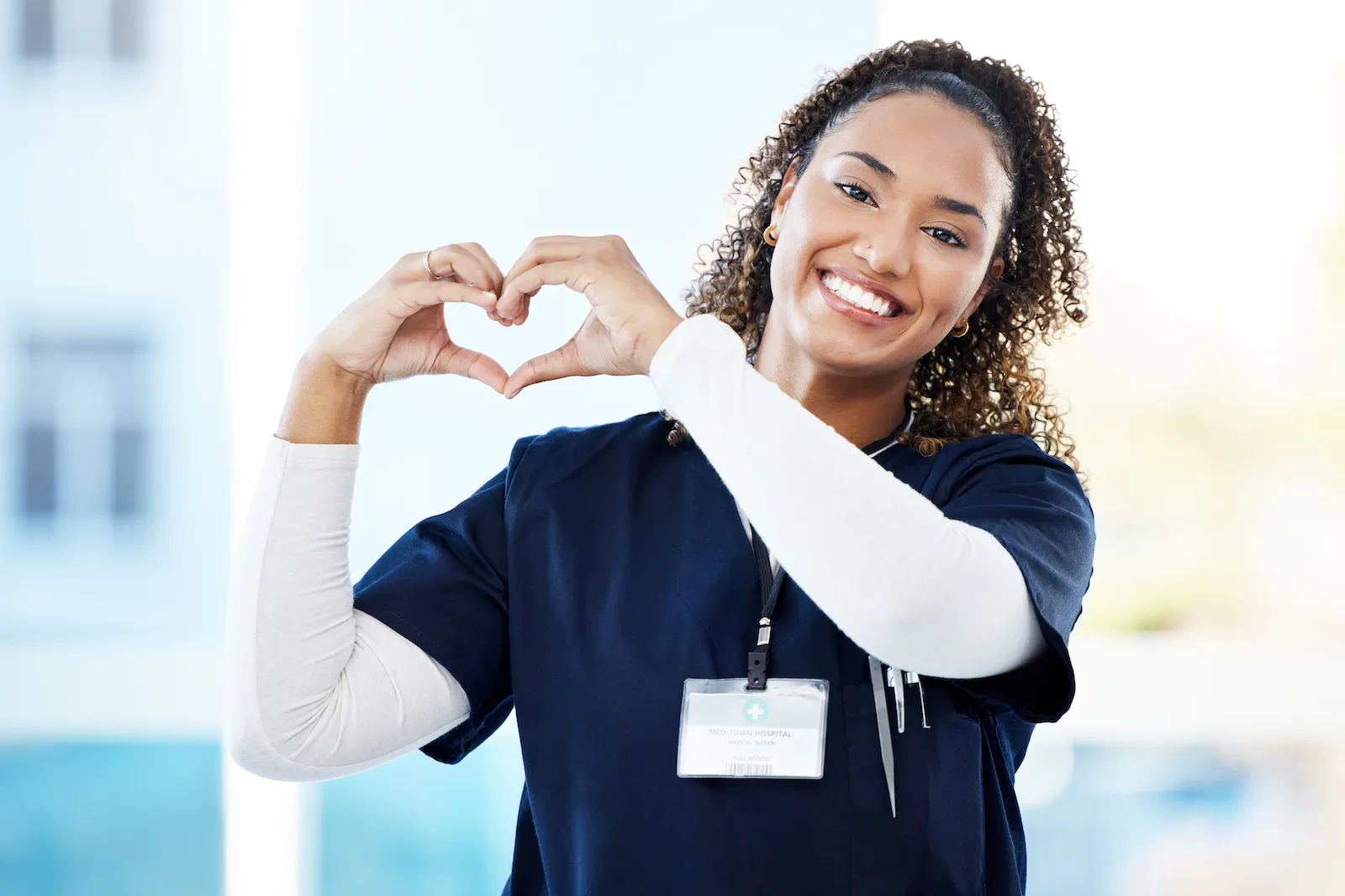 Smiling nurse in scrubs making a heart shape with her hands