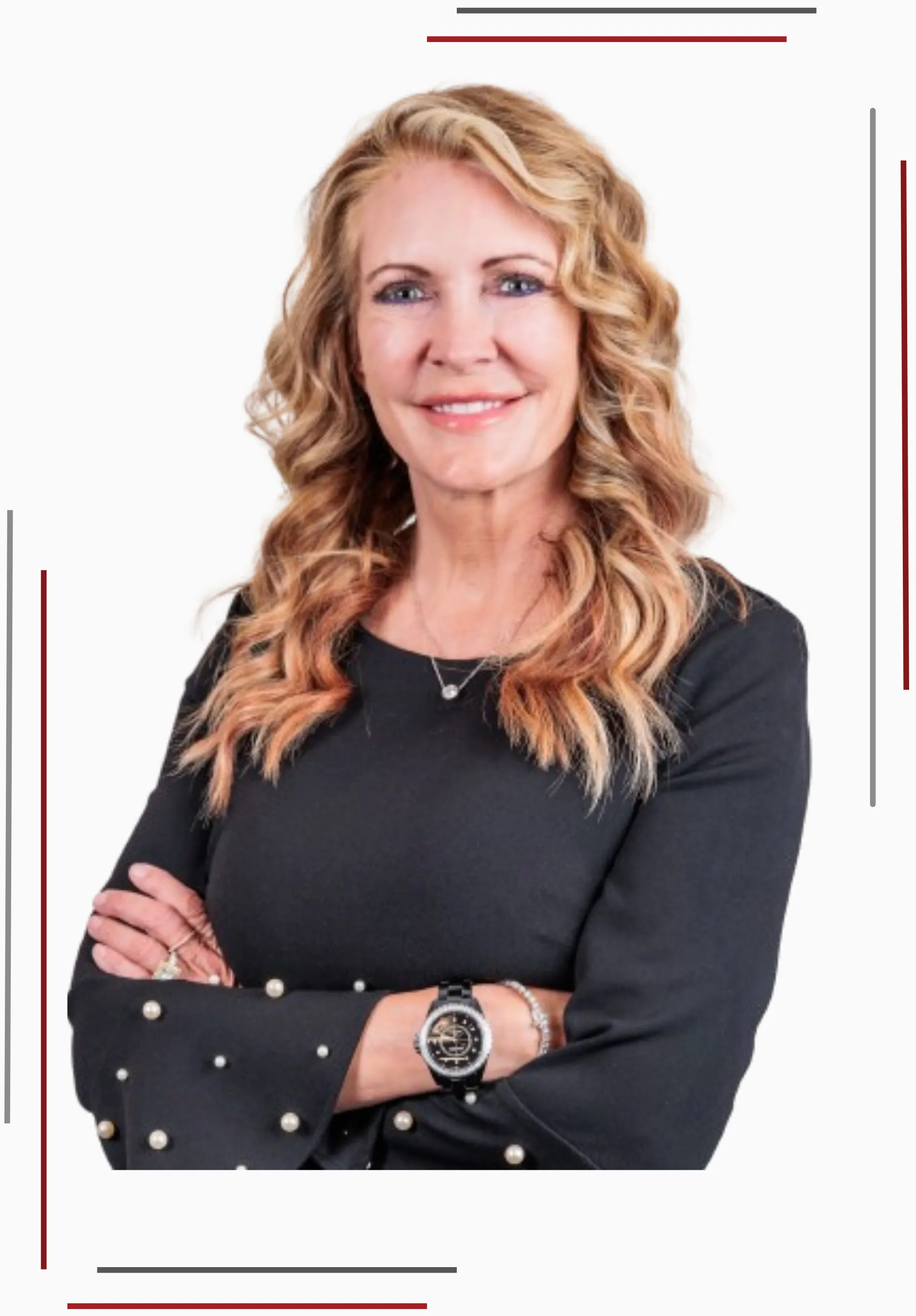 Professional woman with blonde curly hair wearing a black dress with pearl accents, crossing her arms, smiling confidently, wearing a watch and jewelry.
